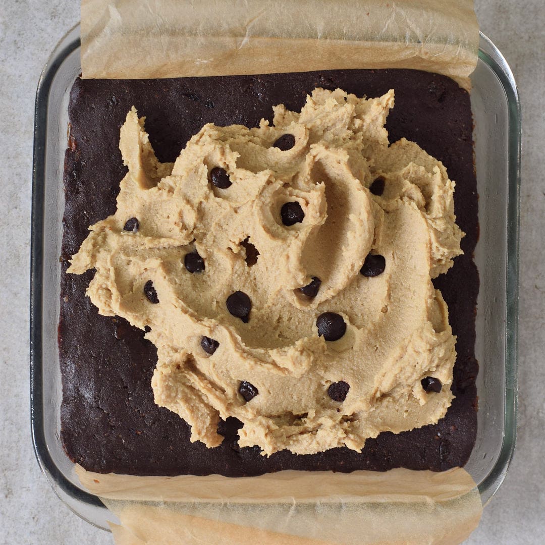 Veganer und glutenfreier Keksteig mit Schokoladenstückchen auf Brownie Boden in einer Form