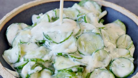 Joghurt Dressing mit Dill wird über Gurkensalat gegossen