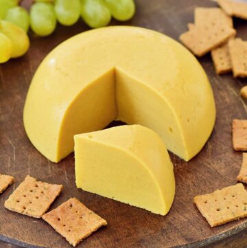 Bester veganer Käse (selbstgemacht) mit Crackern und Trauben auf rundem Holzbrett