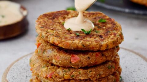 Ein Stapel rote Linsen Bratlinge mit cremiger weißer Soße auf Löffel