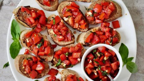 Hand greift nach Bruschetta auf großem weißen Teller
