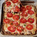 Hand greift nach einem Stück Low Carb Zucchini Pizza mit Tomaten und veganem Käse