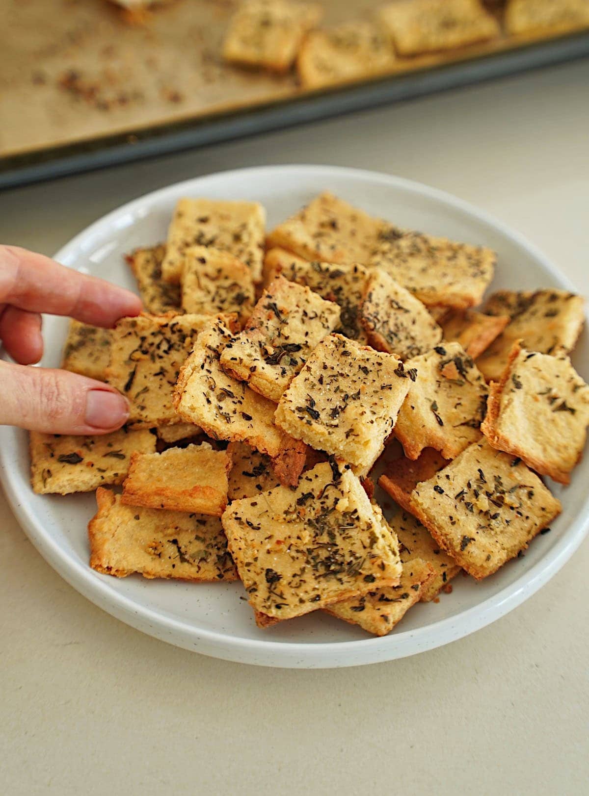 Hand greift nach Kichererbsen-Cracker auf weißen Teller