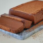 angeschnittener Schokoladen Puddingkuchen auf Steinplatte mit Kakaopulver obendrauf