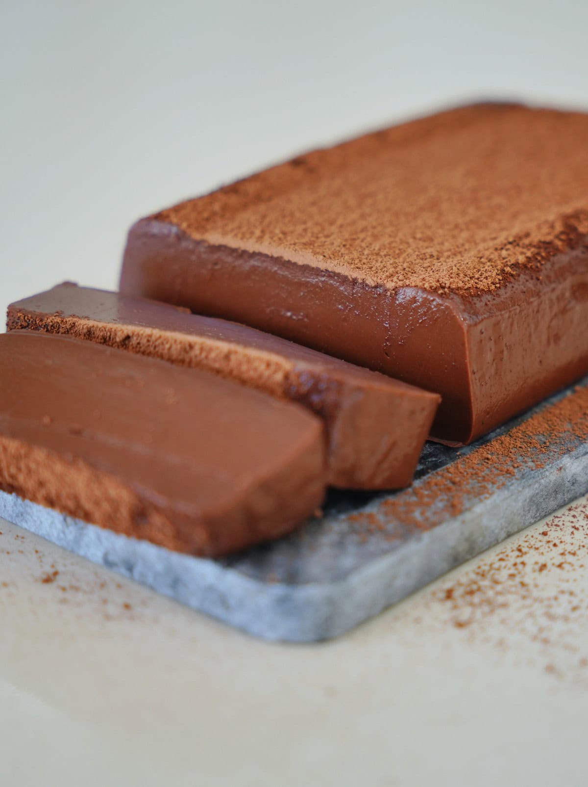 angeschnittener Schokoladen Puddingkuchen auf Steinplatte mit Kakaopulver obendrauf