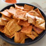 Schwarze Schale, gefüllt mit knusprigen, goldbraunen, rechteckigen Linsencrackern, bestäubt mit Paprika