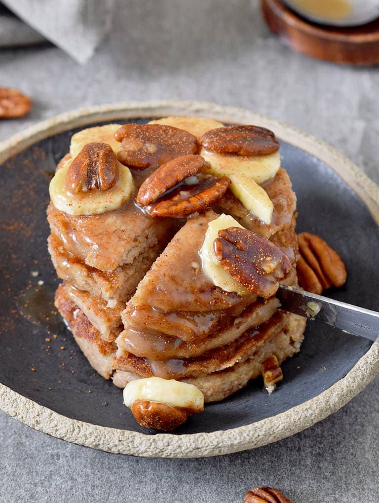 cutting into a stack of 5 pancakes with banana and pecans