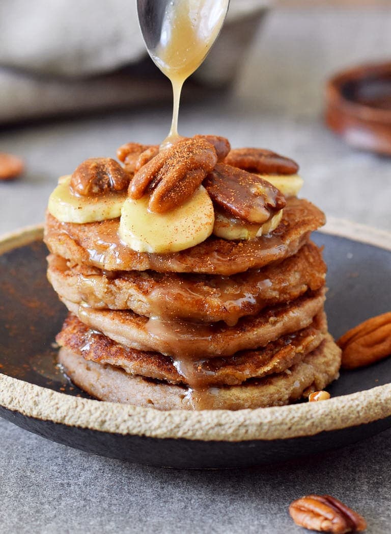 stack of 5 vegan oat flour pancakes with pecans and banana with maple drizzle