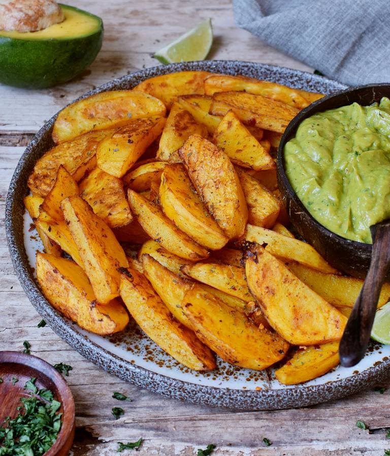 Close up of thick potato fries in a bowl with creamy guacamole