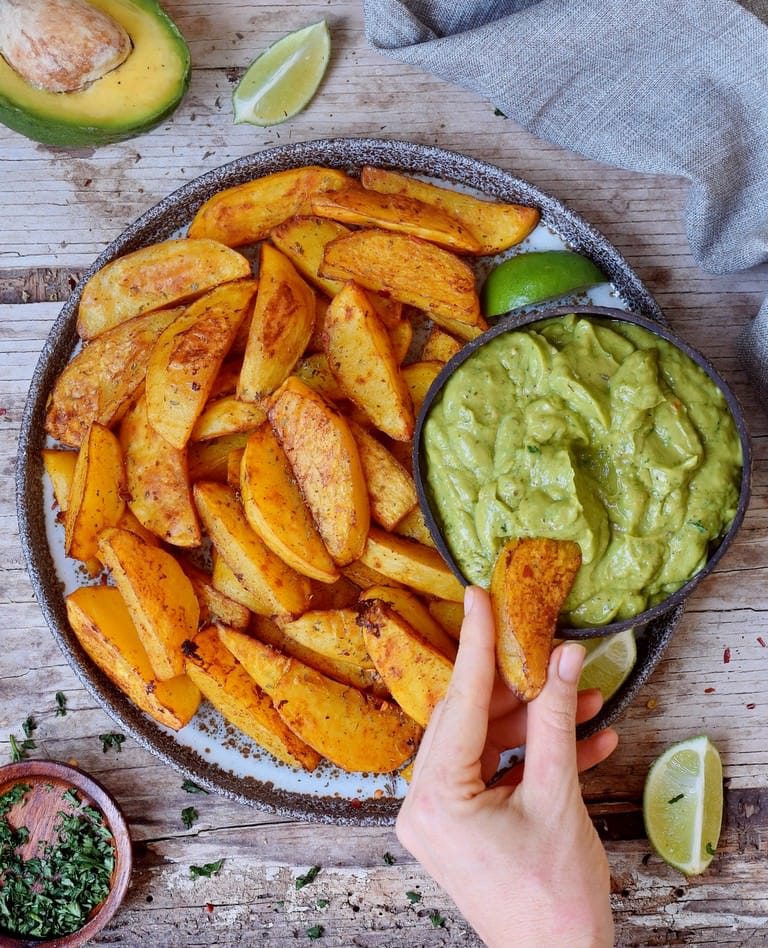 Oven-baked potato wedges in a bowl with creamy guacamole