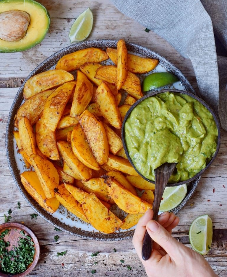 Oven-baked potato wedges on a plate with creamy guacamole