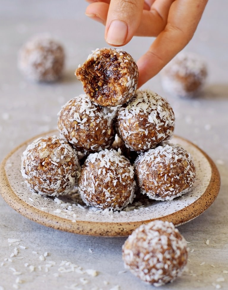 hand grabbing an energy ball from a small plate coated with desiccated coconut