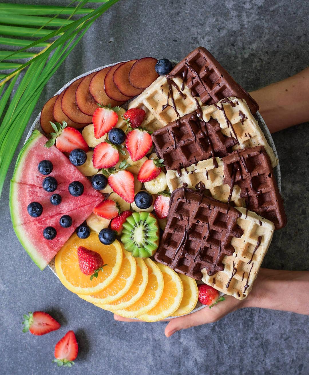 Homemade eggless vanilla waffles with fruits, a chocolate sauce, arranged on a board