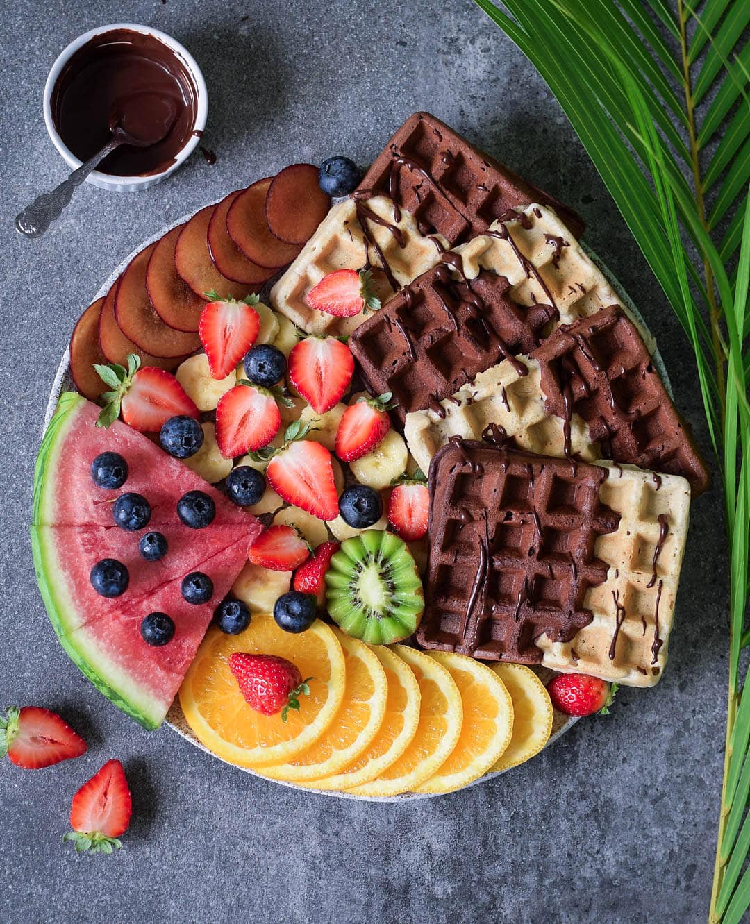 Gluten-free vegan waffles with fruits, a chocolate sauce, arranged on a board