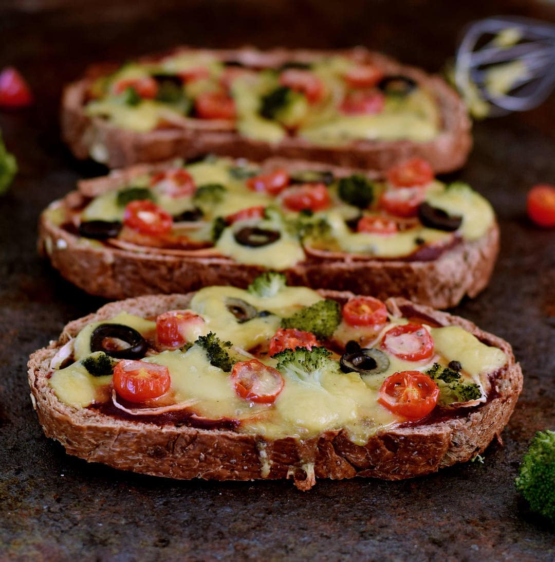 Plantbased queso on three toasts with olives, tomatoes and broccoli