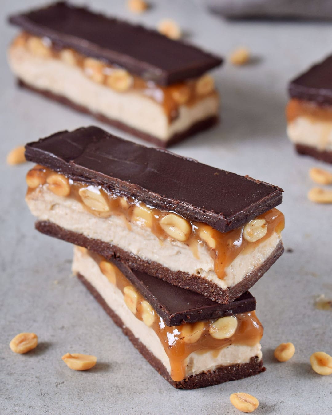Stack of homemade caramel chocolate candy bars with a brownie base, cashew cream, peanut caramel and dairy-free chocolate