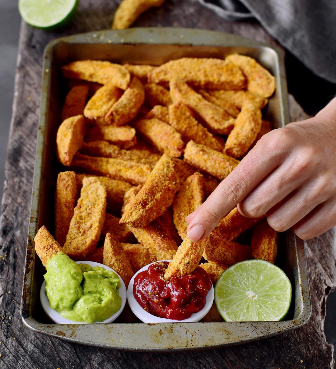 Eating oven-baked vegan parmesan potato wedges with guacamole dip and ketchup