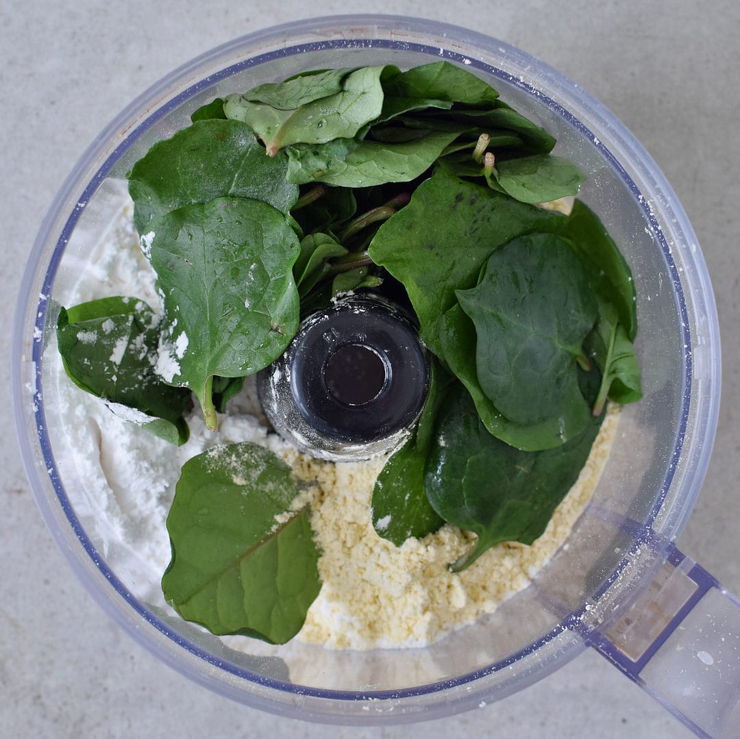 Gluten-free flour, water, and baby spinach in a food processor