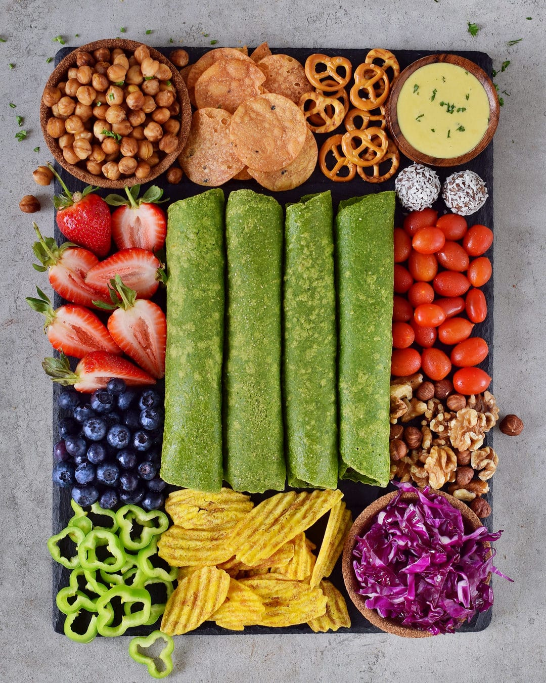 4 green spinach tortilla wraps on a snack platter with fruit, vegetables, nuts, and chips