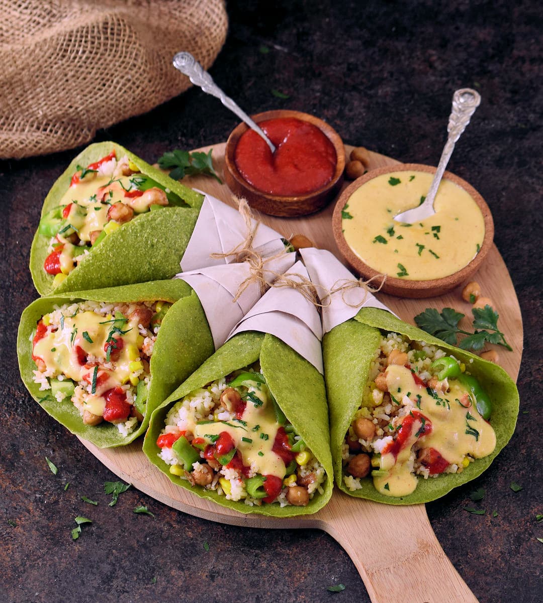 4 green wraps filled with rice, veggies, and chickpeas on a platter with 2 dips