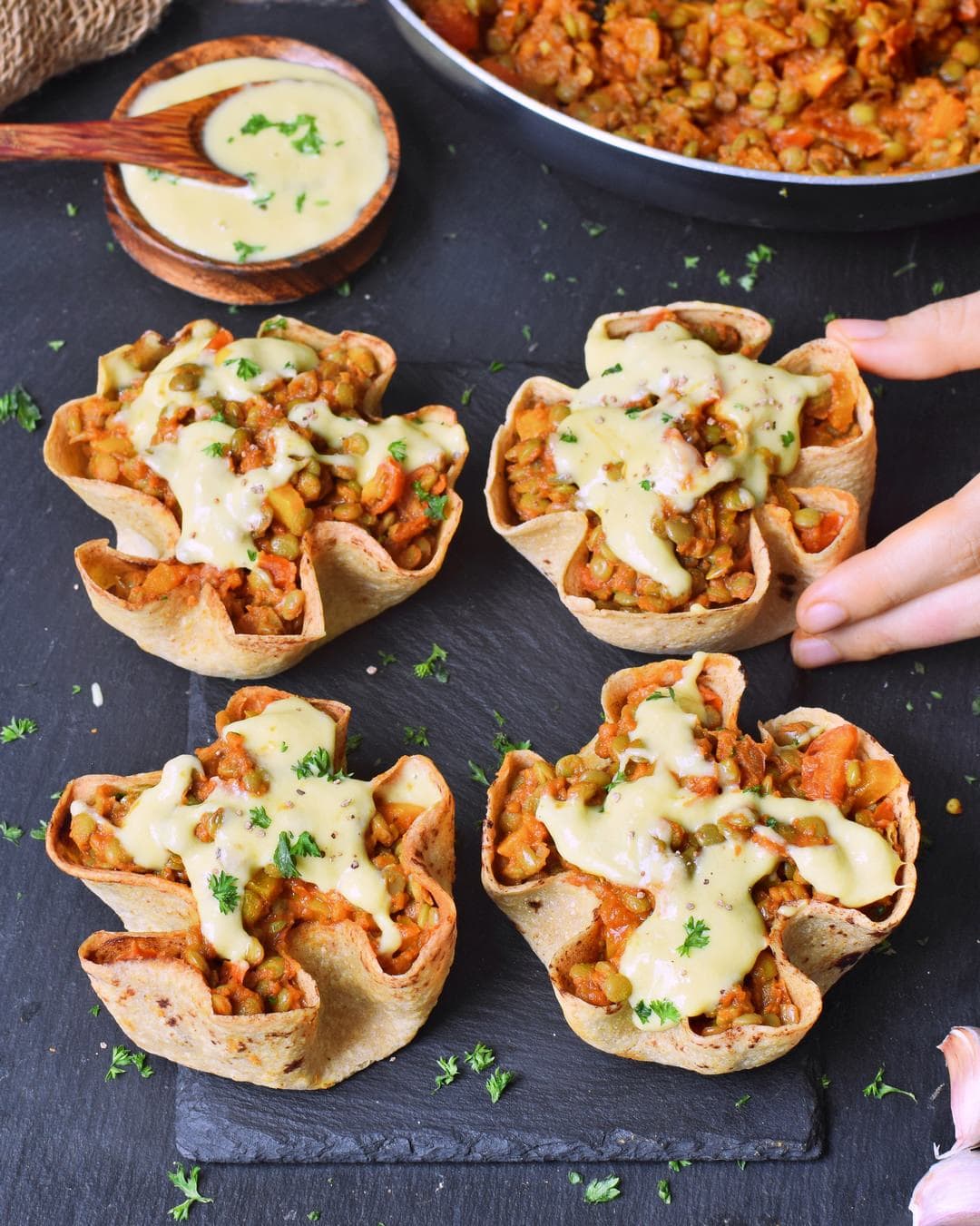 hand grabbing one stuffed taco cup with lentil mixture and vegan cheese sauce