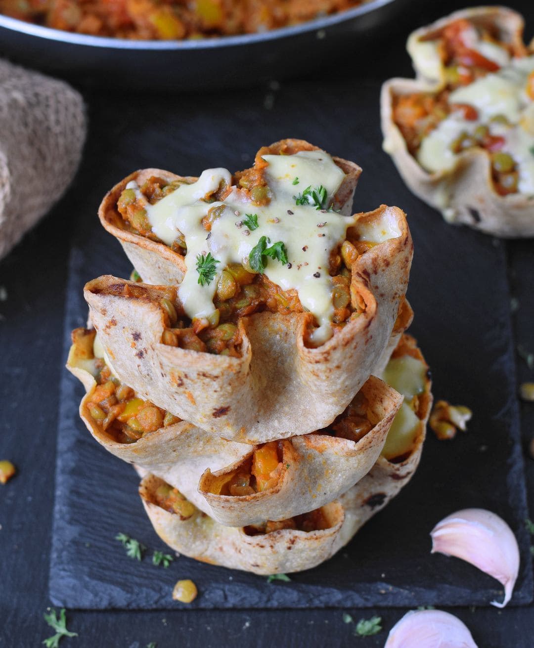A stack of three homemade tortilla bowls filled with lentil veggie mixture and vegan cheese sauce
