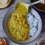 vegan lentil dal with carrots and rice on a plate with a ladle
