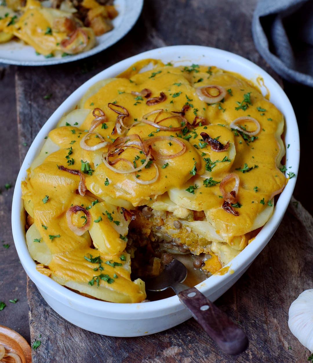 potatoes au gratin with pumpkin and protein-rich lentils in a round baking dish with fried onion rings