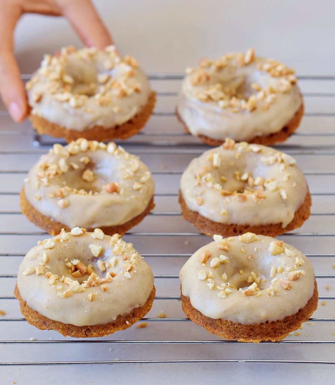 hand grabbing vegan carrot cake donuts with gingerbread flavor and frosting on a wire rack