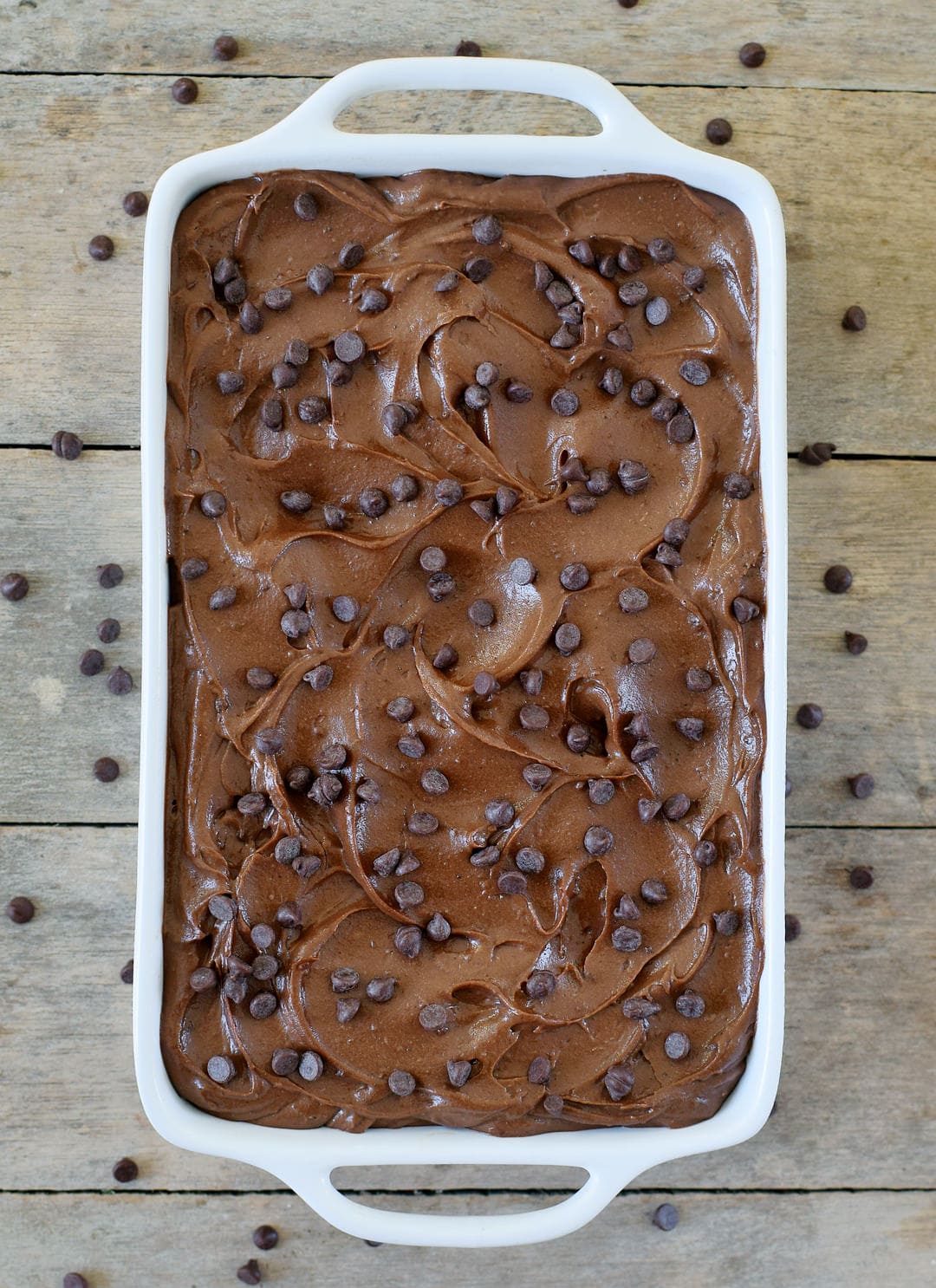 Chocolate batter in a baking dish with sweet potato frosting and mini chocolate chips