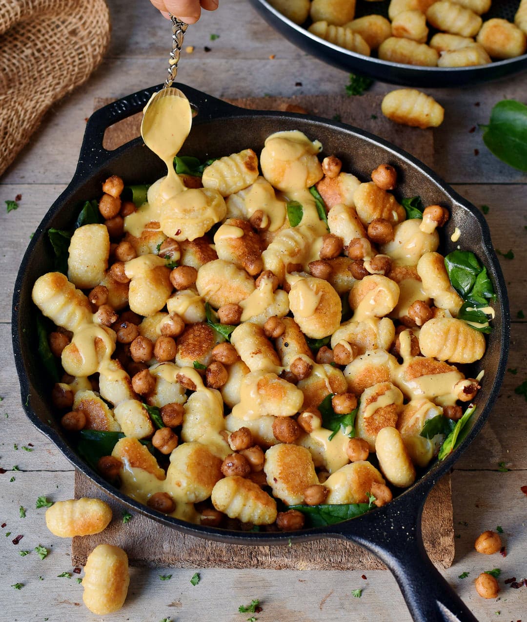 Homemade gluten-free gnocchi with roasted chickpeas spinach and vegan cheese sauce in a black skillet