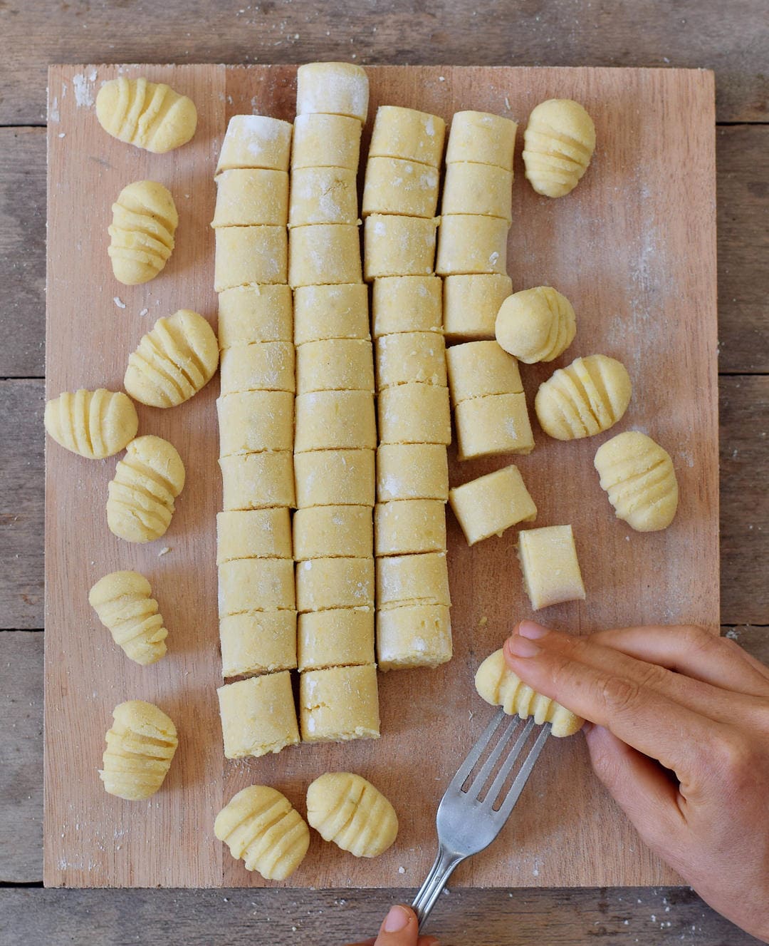 Rolling homemade Italian potato pasta over a knife on a wooden cutting board