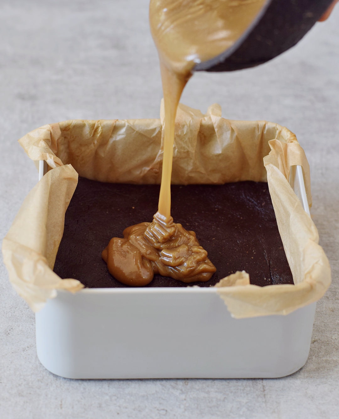 pouring vegan caramel onto brownie base