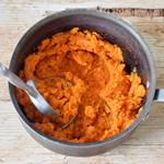 mashed sweet potato in a black pot with a potato masher