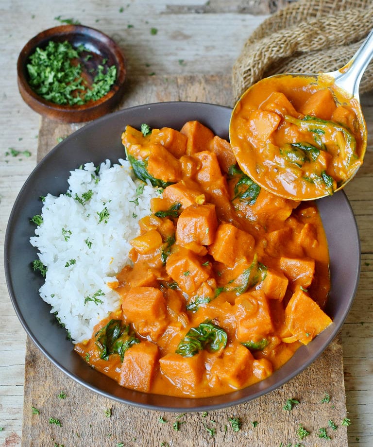 Healthy Vegan Sweet Potato Curry with rice and spinach in a bowl with a laddle