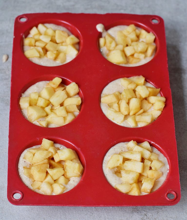 Teig und Apfelstücke für Apfelmuffins in einer roten Muffin-Silikonform