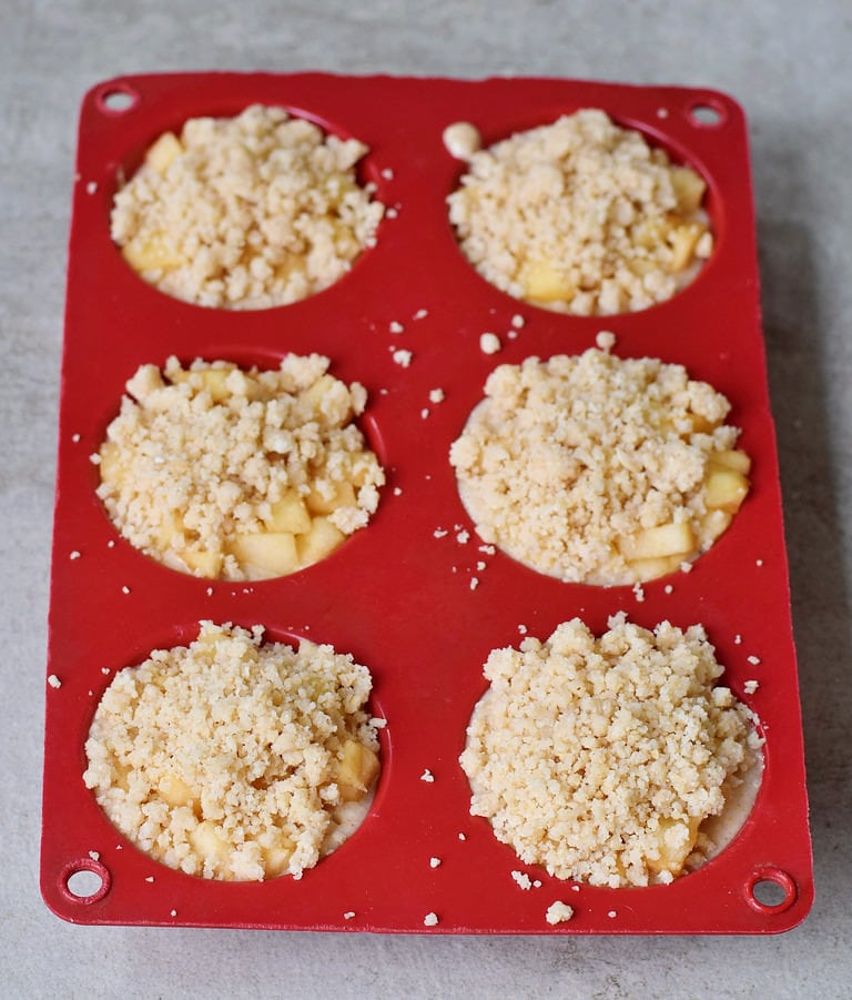 Teig, Apfelstücke und Streusel für Apfelmuffins in einer roten Muffin-Silikonform