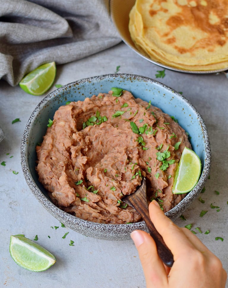 Instant Pot Refried Beans in a blue bowl with tortillas in the background