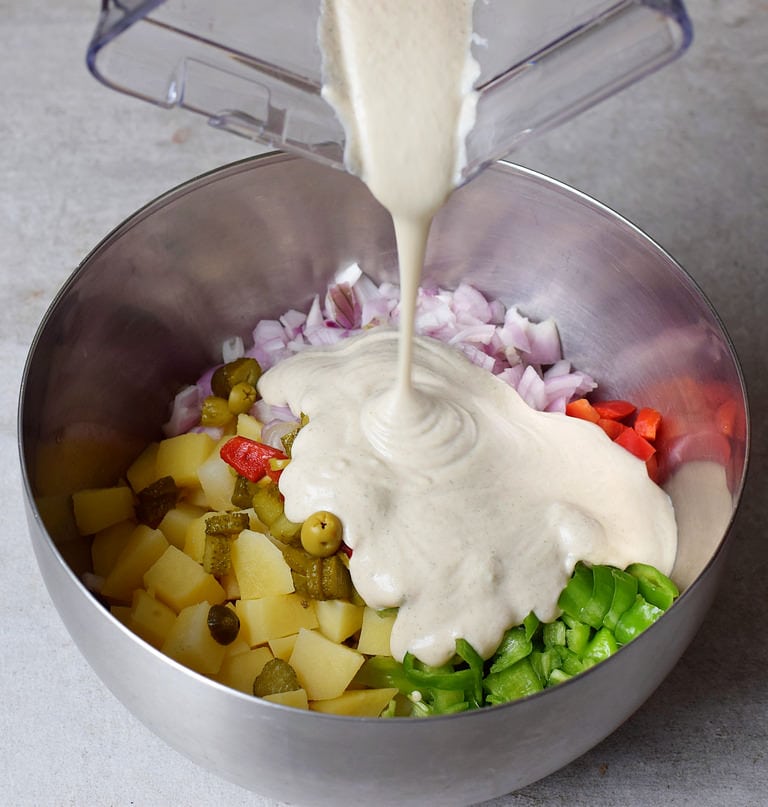 pouring oil-free dressing into a bowl of veggies and potatoes