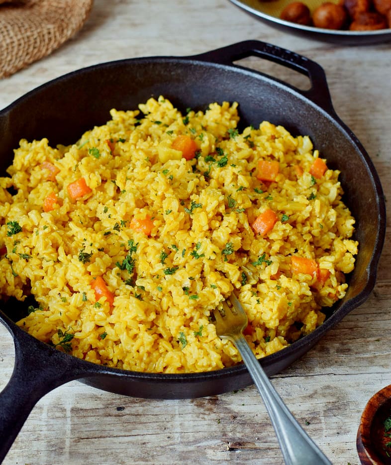 Goldener Kurkuma Reis mit Gemüse und Kokosmilch in einer schwarzen Pfanne mit Gabel