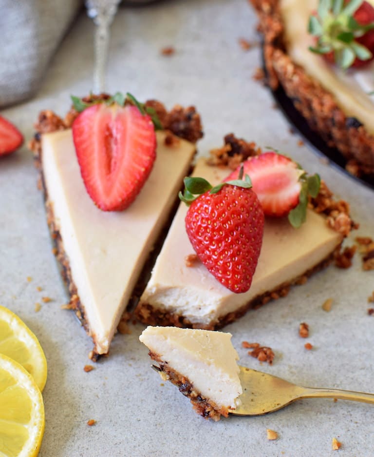 Two slices of vegan lemon cheesecake tart with granola crust and strawberries