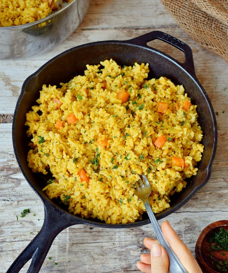 Yellow coconut turmeric rice in a black skillet with a fork