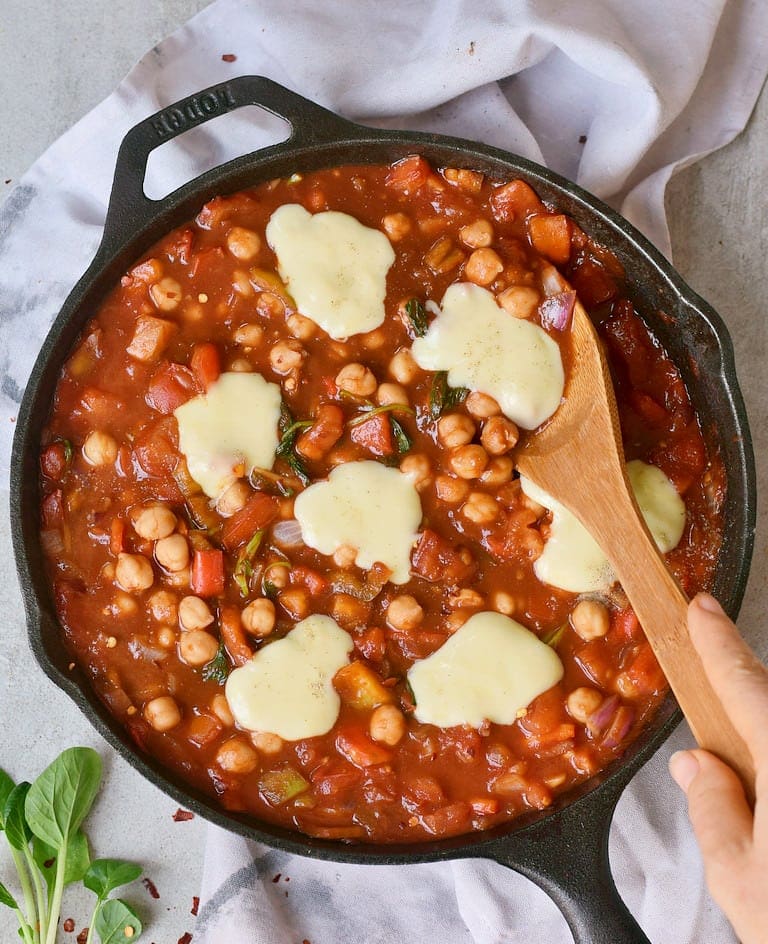 Egg-free tomato stew with plant-based cheese in a black pan