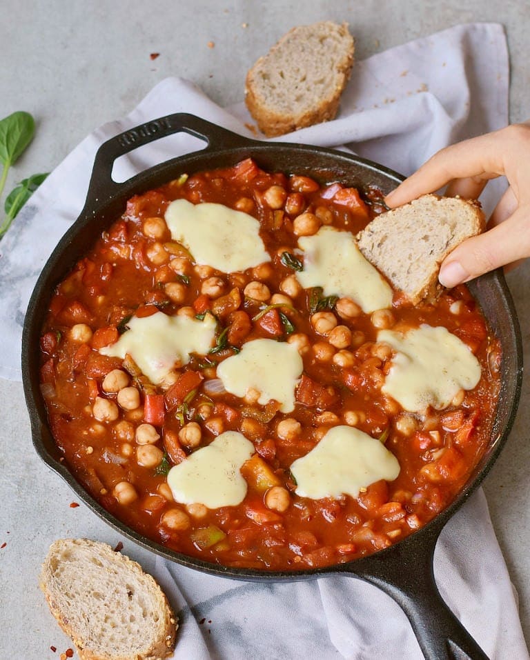Hearty egg-free Shakshuka with vegan cheese and chickpeas in a black pan