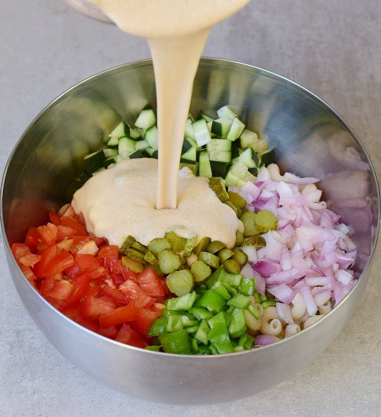 pouring oil-free dressing without mayo over veggies and noodles