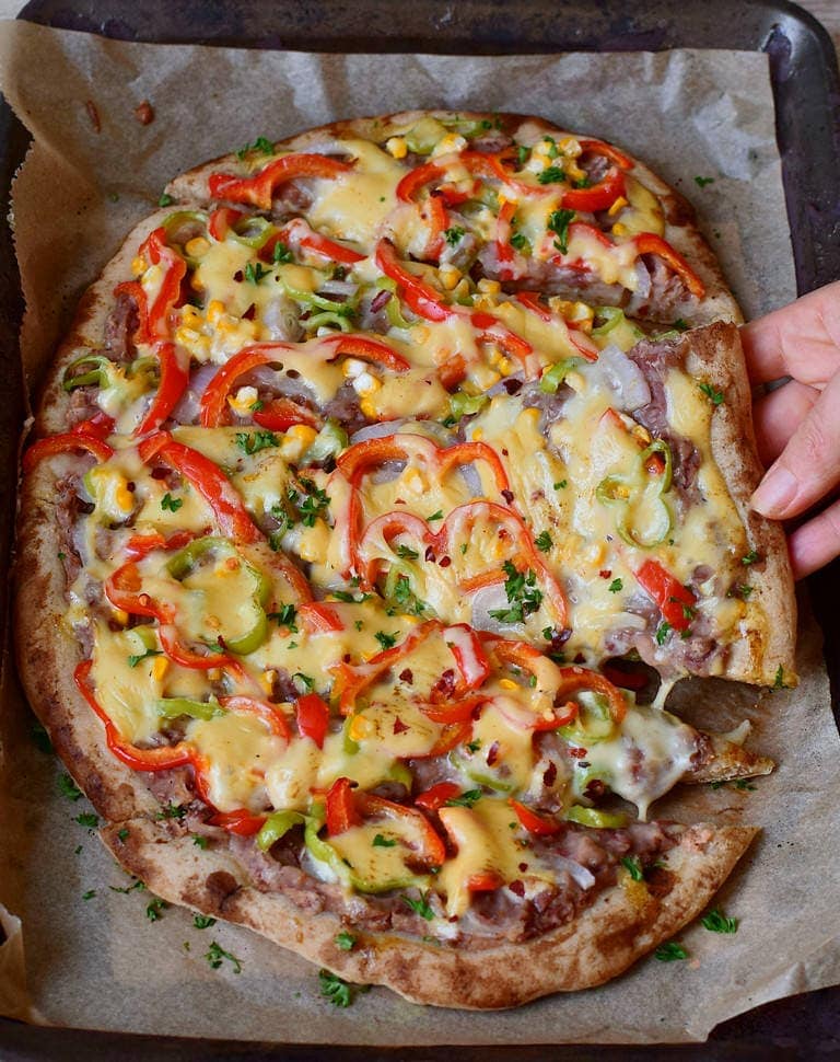 Hand greift nach mexikanischer Pizza mit Bohnenmus Paprika Mais und veganem Käse