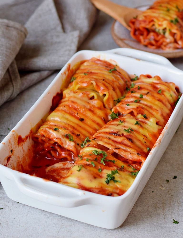 Lasagna roll ups in a baking dish with vegan cheese