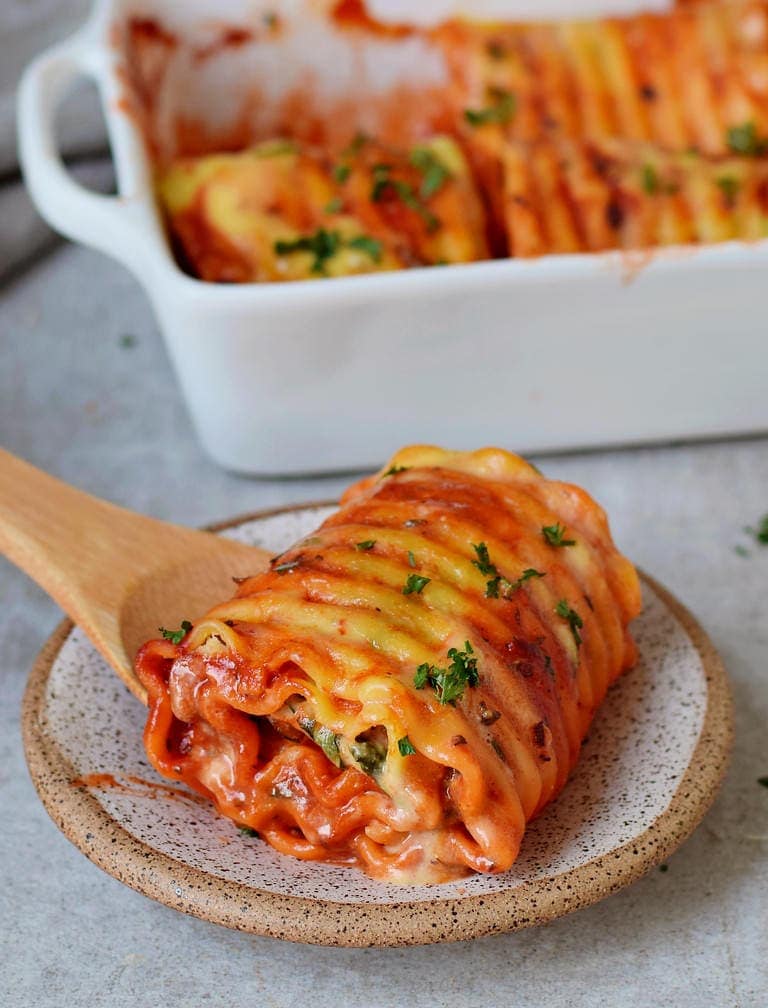 One lasagna roll up in a baking dish with vegan cheese