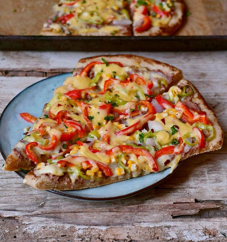Two pieces of Mexican Pizza recipe with corn refried beans peppers and vegan cheese