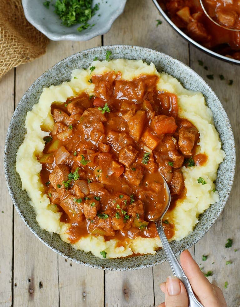 Eating vegan goulash with soy protein in a bowl over mashed potatoes